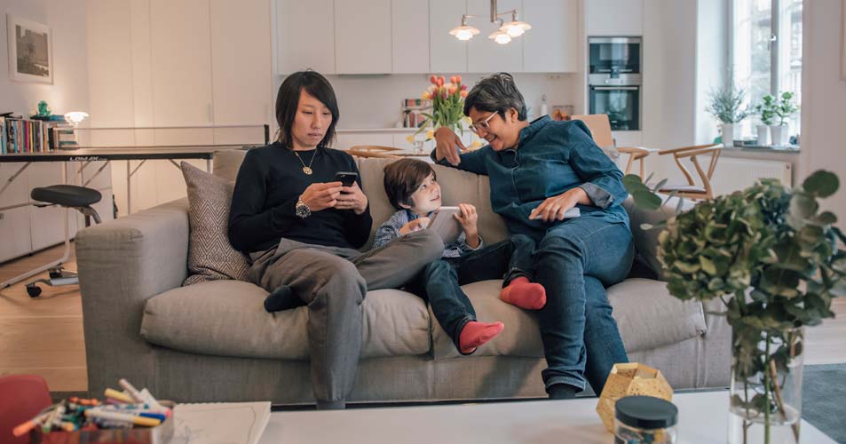 Familj sitter i soffa och använder iPhones och iPad, en del av det digitala livet många lever idag